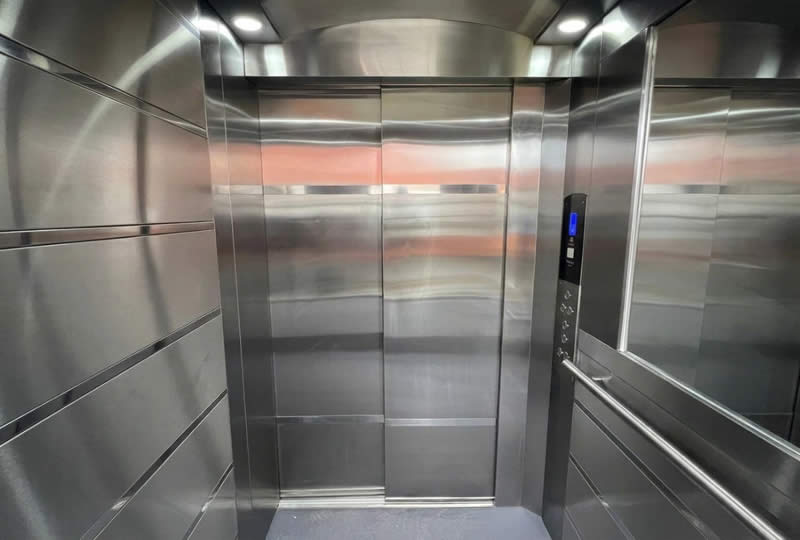 Descubra un interior de ascensor moderno en acero inoxidable con espejo, panel de control y elementos de seguridad en Bogot&aacute;, Colombia. Ascensores Fahenn